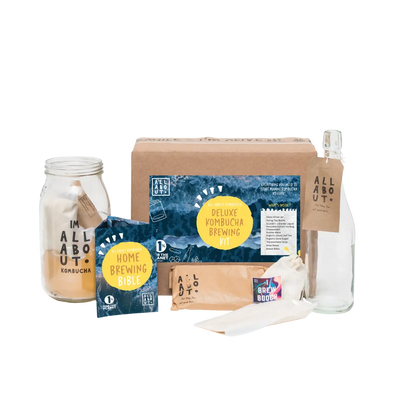 Home kombucha brewing kit displayed on a white background, including a fermentation jar, glass bottle, tea bags, brewing accessories and a brewing guide booklet