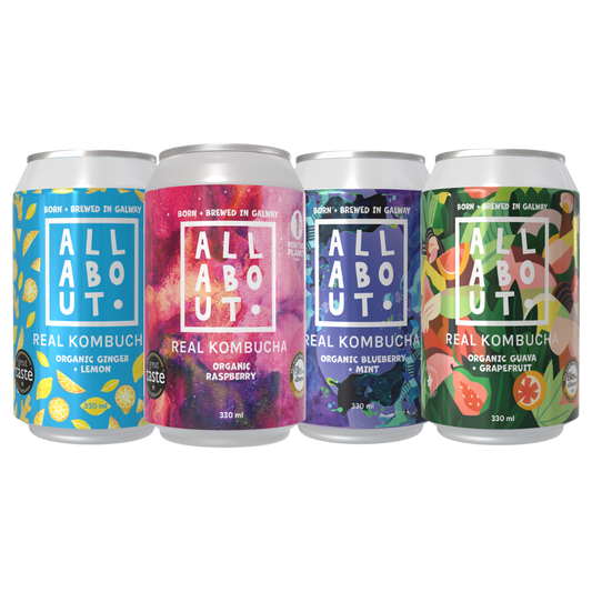 Four aluminum cans of All About Kombucha arranged side by side on a white background. The labels feature colorful fruit and flavor designs: blue lemon, pink raspberry, purple mint, and green guava/grapefruit.
